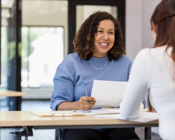 The office manager holds onto a resume while speaking with the new intern they are considering.